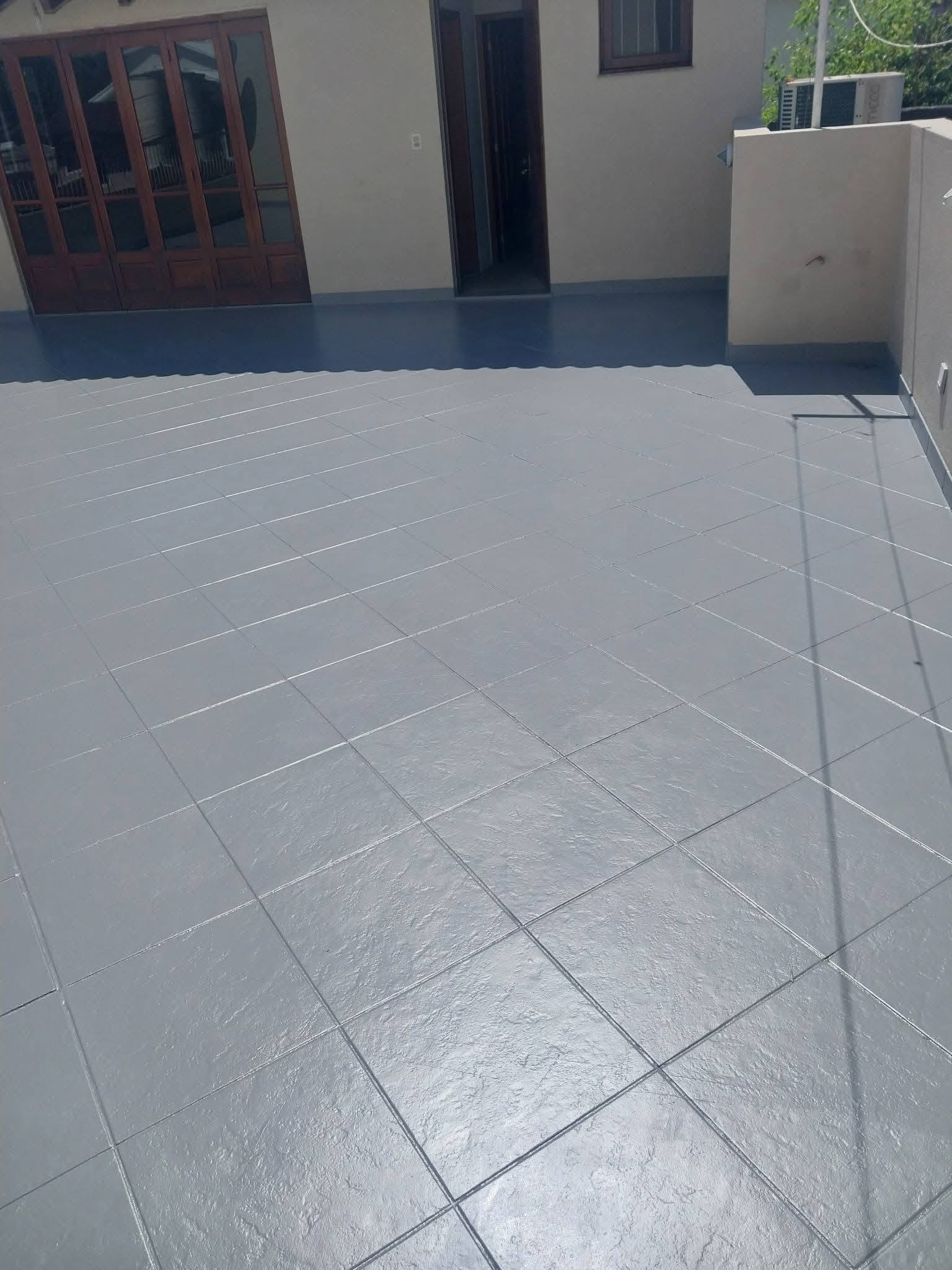Terraço amplo de cobertura com impermeabilização de piso em tom cinza-escuro com juntas marcadas, janelas de madeira ao fundo, fotografia realista