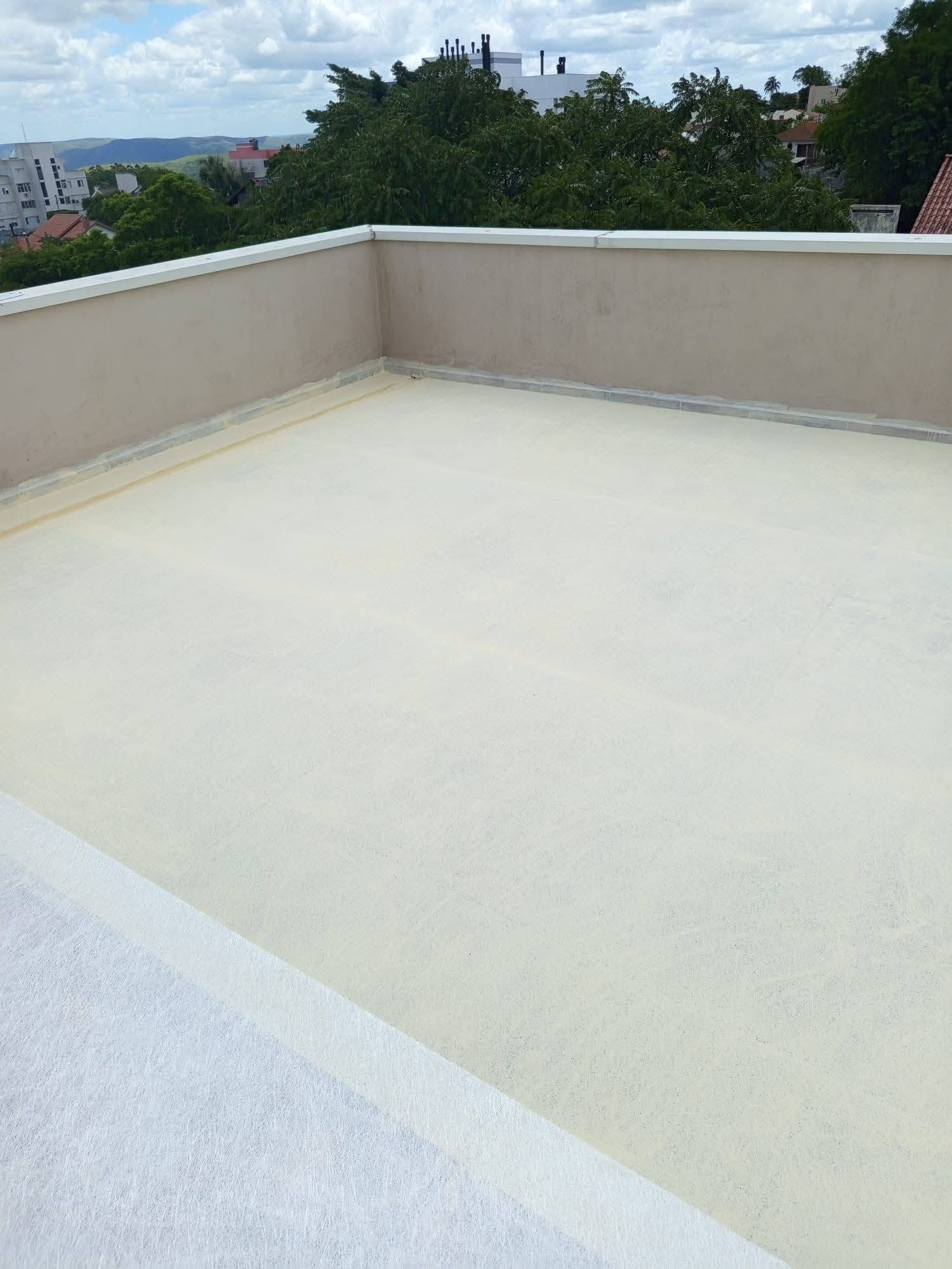 Laje de cobertura impermeabilizada com manta líquida cor creme, acabamento uniforme com juntas demarcadas, vista de telhados e árvores ao fundo, fotografia realista