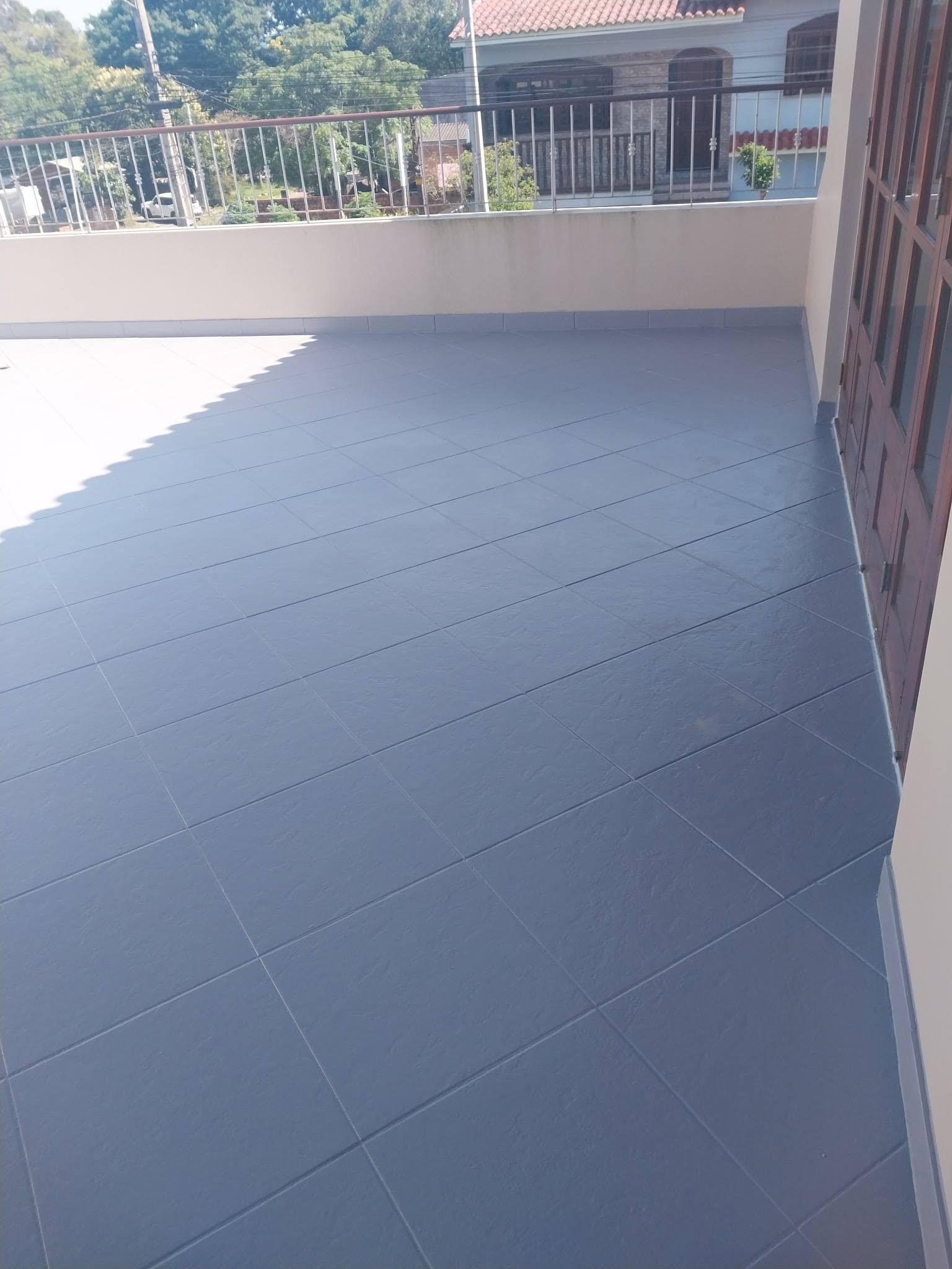 Sacada de apartamento com impermeabilização de piso concluída em tom azulado claro e escuro contrastando ao sol, grades de ferro ao fundo, fotografia realista