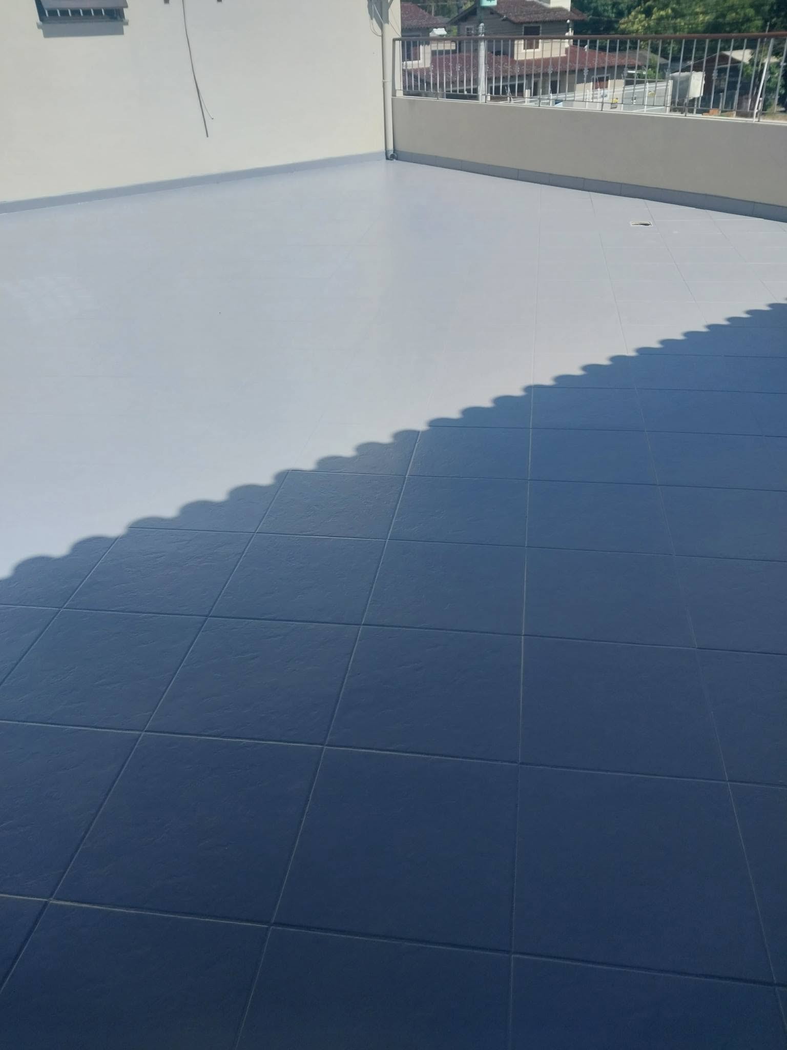 Piso de terraço impermeabilizado com acabamento azul-acinzentado em placas demarcadas, portas de madeira ao fundo, fotografia realista